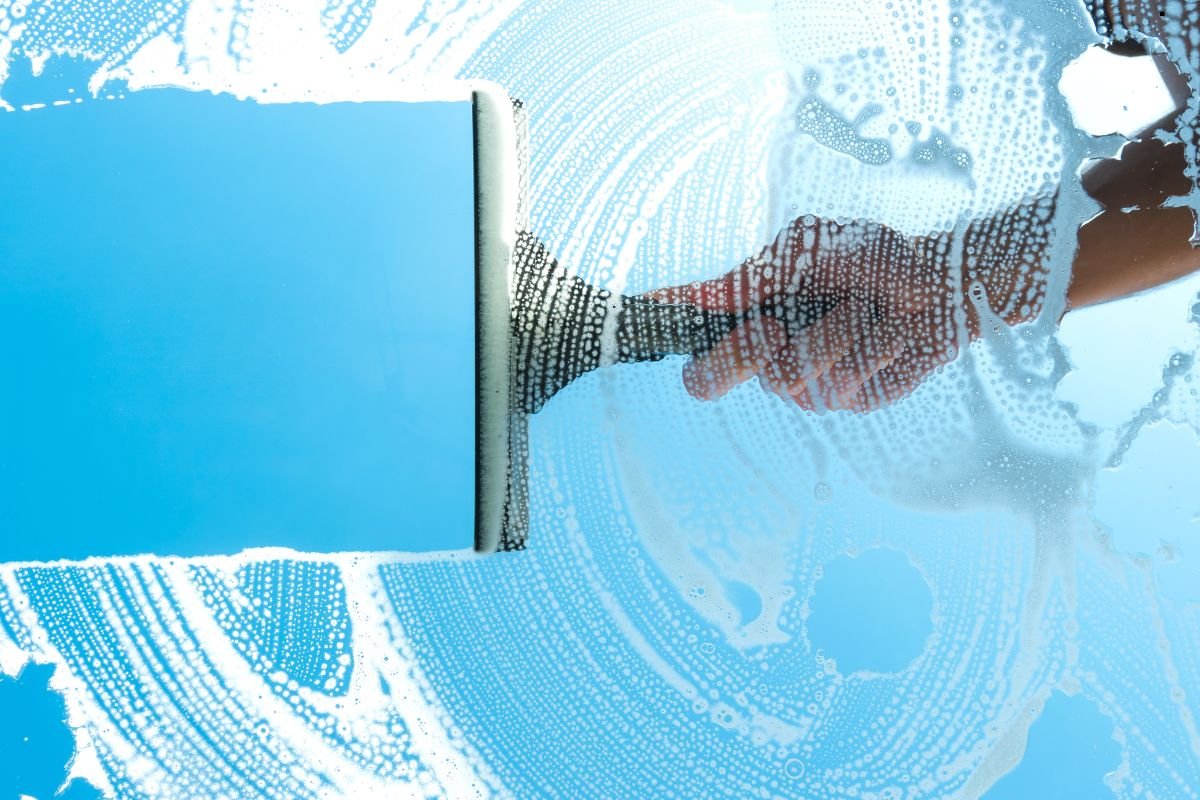 An individual is using a squeegee to clean a window, demonstrating proper window cleaning techniques.