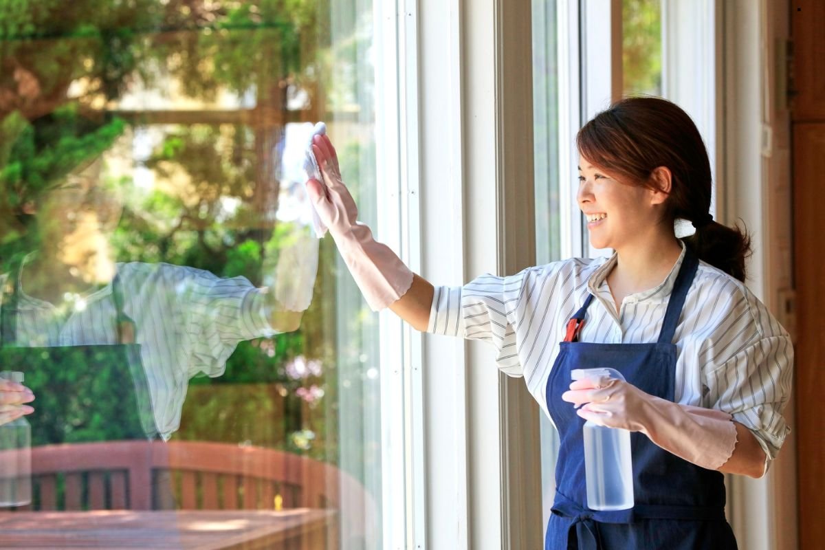 A woman wearing an apron is focused on cleaning a window, enhancing the brightness of the room.