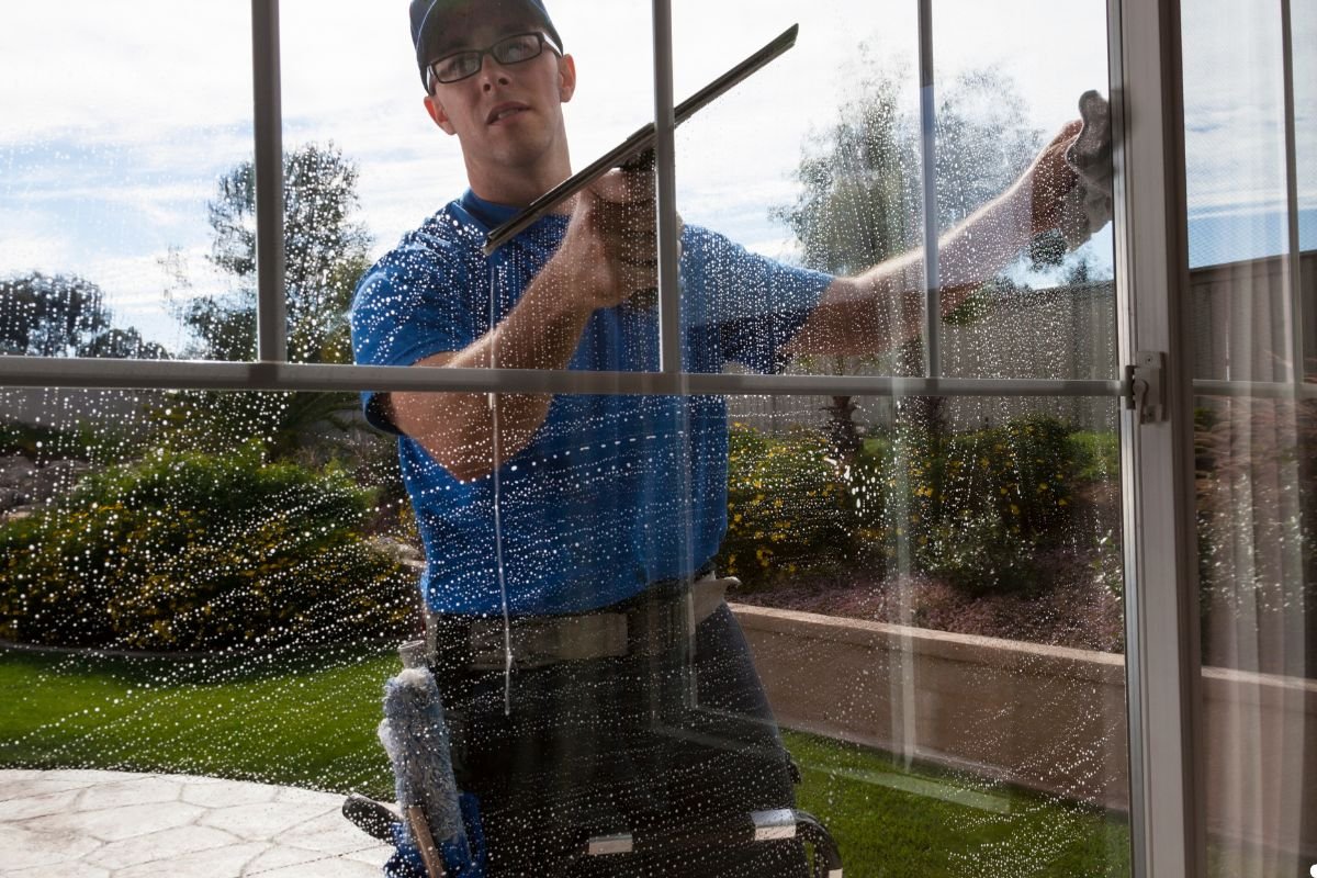 A man in a blue shirt is cleaning a window using a window cleaner, focusing on removing dirt and streaks.